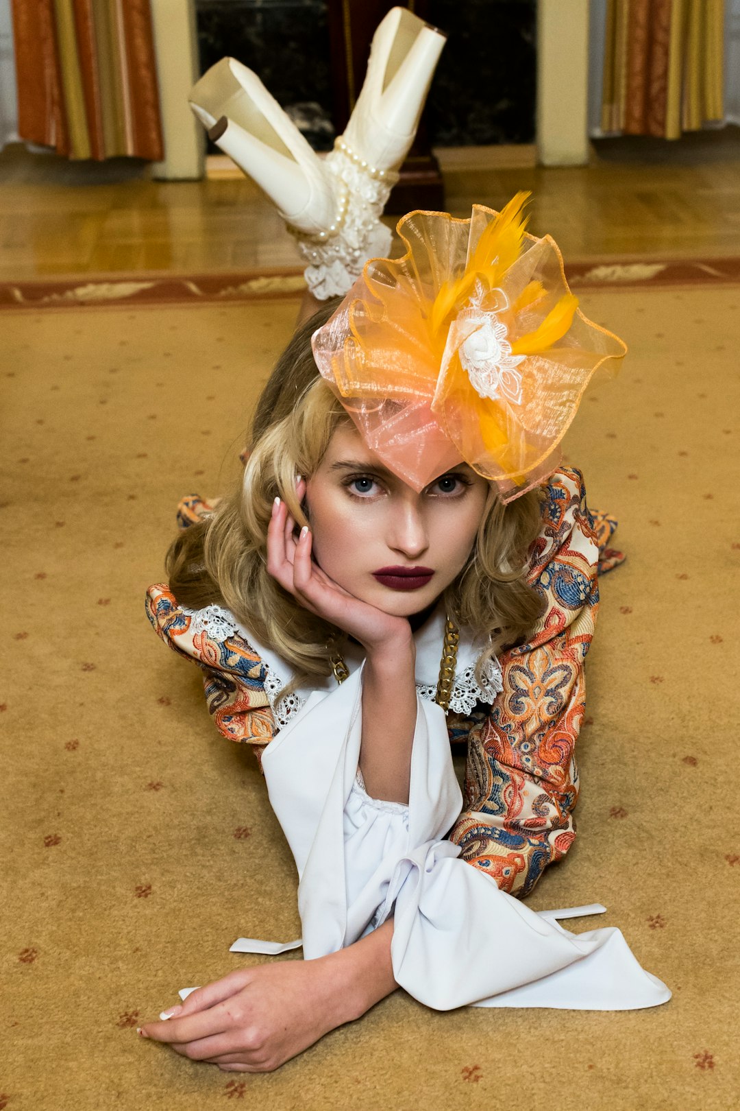 Woman wearing an ornate dress, orange fascinator, and high heels.