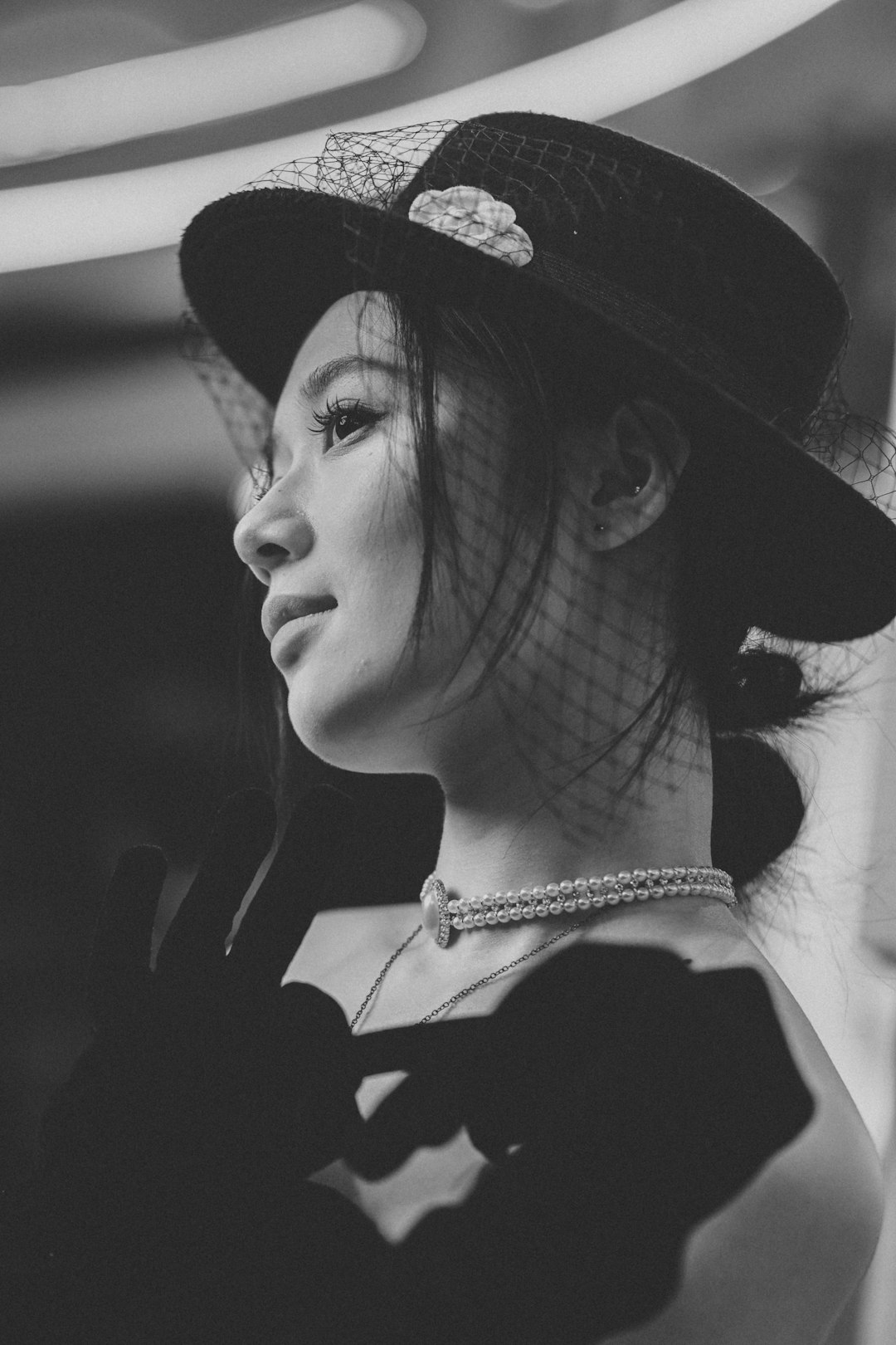 Elegant woman wearing a veiled hat and pearl necklace.