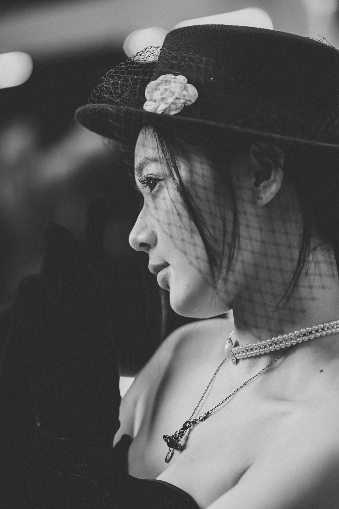 Profile of a woman wearing a hat and pearl necklace.