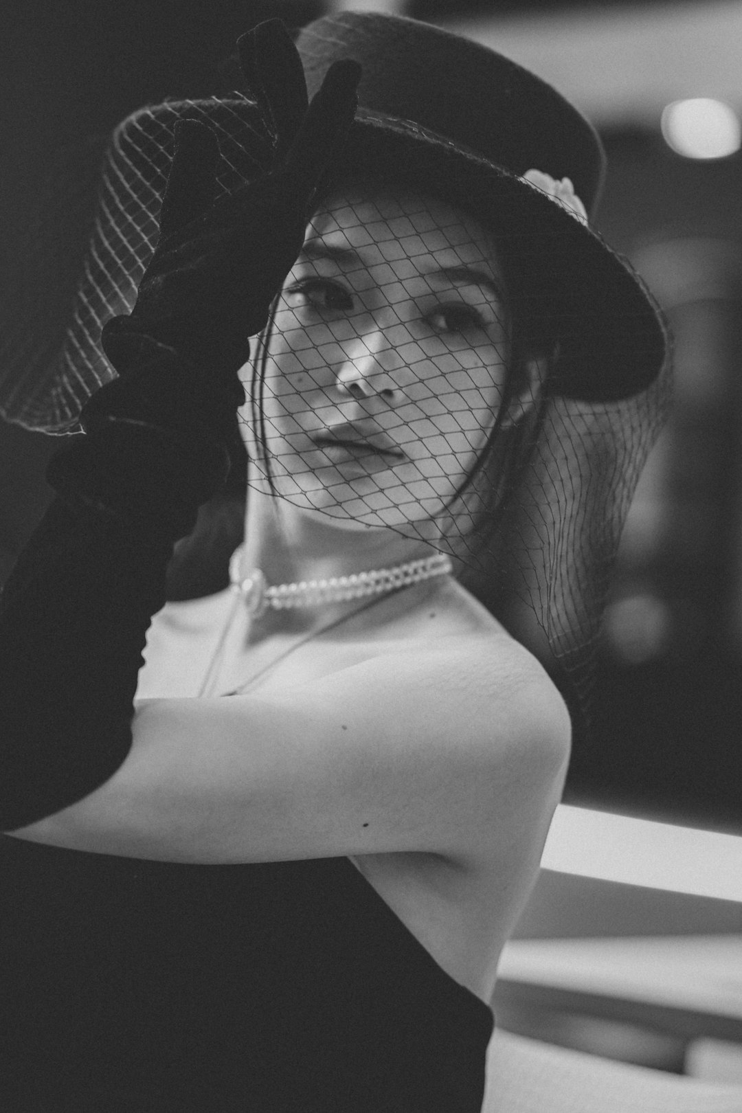 Woman in veiled hat, long gloves, and pearl necklace.